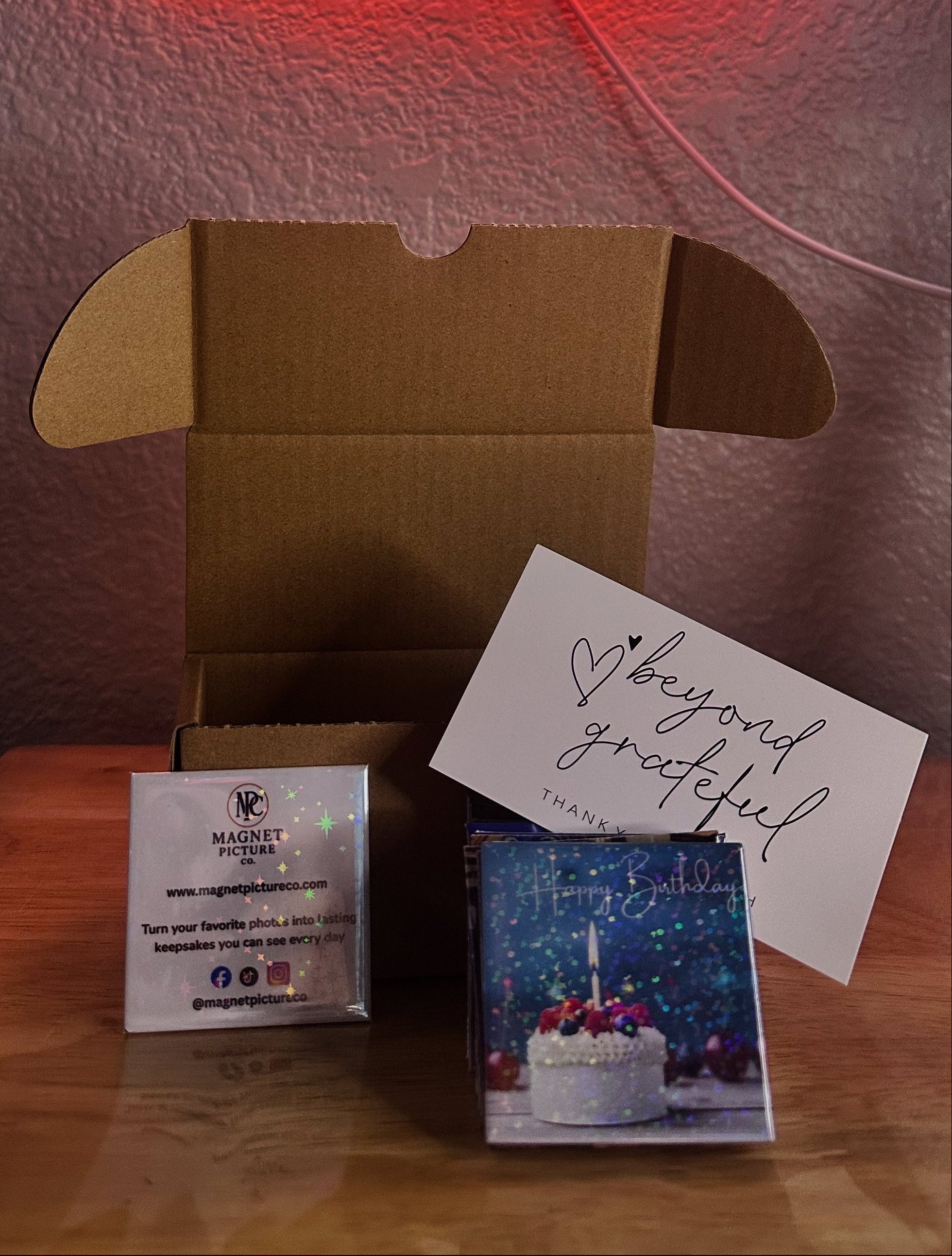 Neon sign with 'Snap Print Stick' text above a cardboard box and items on a table.